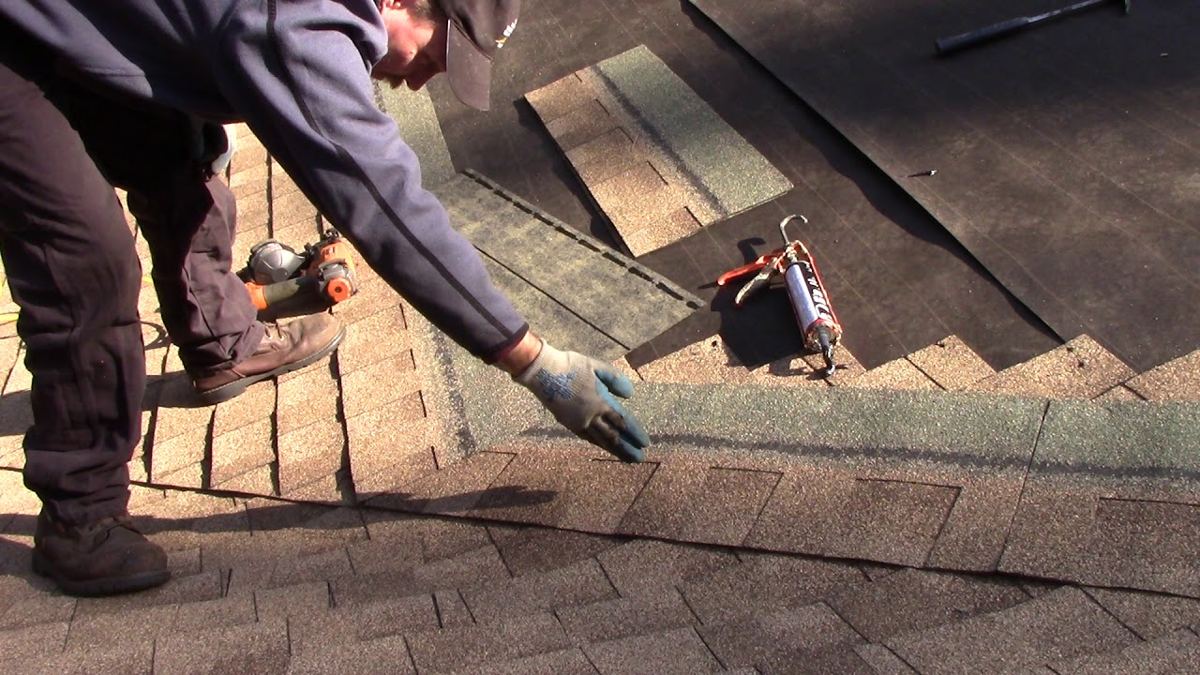 Roofing contractor repairing asphalt shingles and checking roof nail fastening